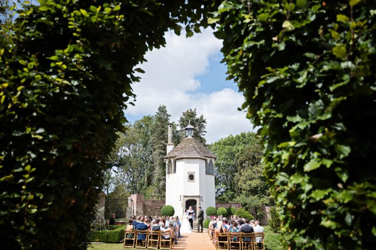 View through a hedge at wedding venue Homme House for a Herefordshire wedding. Guest seated down. Looks romantic.