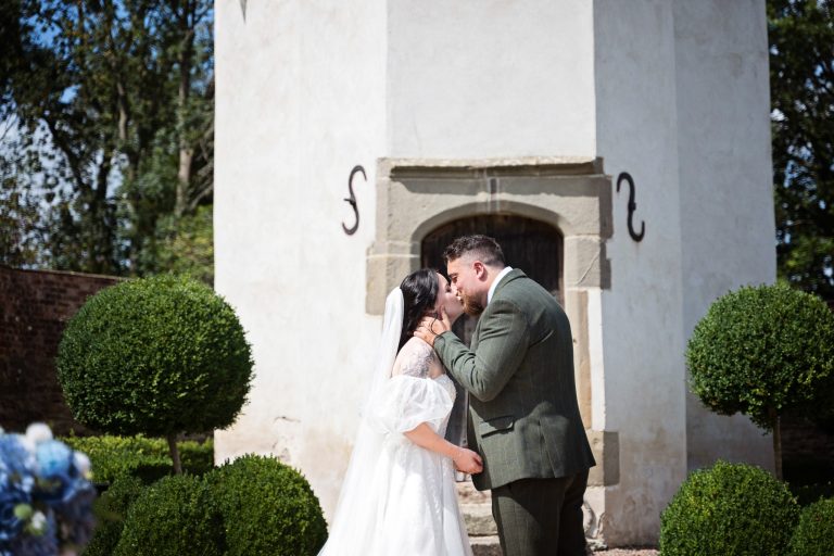 a bride and groom kiss as they are announced husband and wife. A castle is behind them