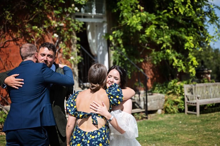 Two wedding guests hugging the bride & groom