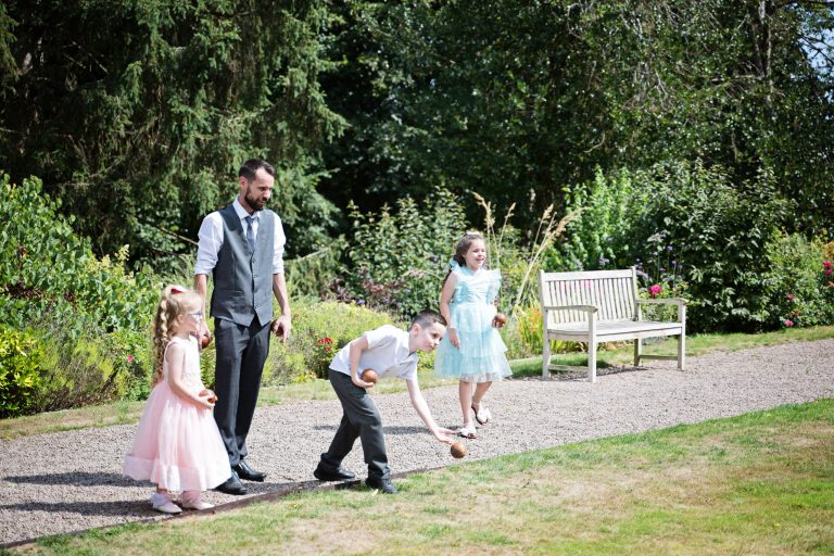 A child throws a patonqe boule with two children and a dad watching