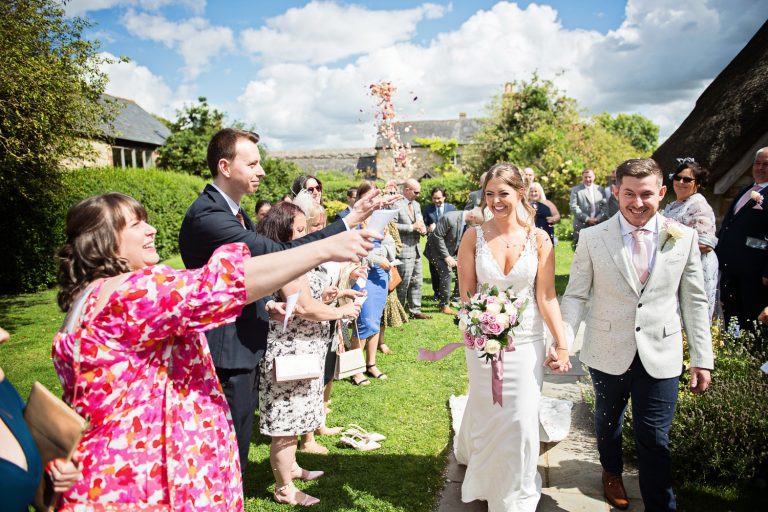 Bride and groom smiling as their guests throw confetti at them