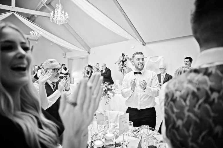B&W image of Wedding guests raising a glass and saying cheers at the end of speeches.