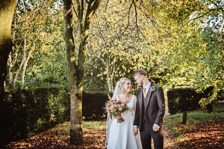 Autumnal photograph of bride and groom holding hands and looking at each other. Natural.