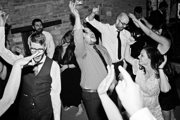 B&W photo of wedding guests enjoying the evening by dancing and hands in the air.