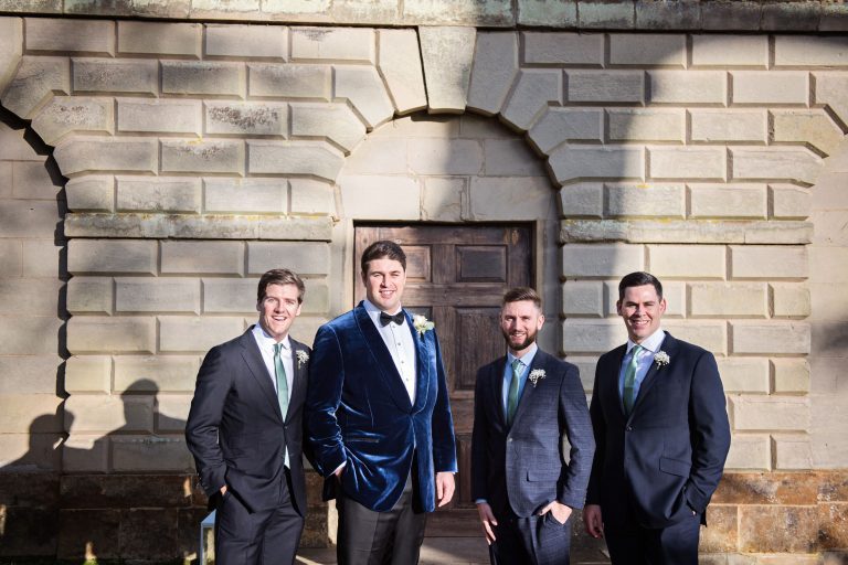 Groomsmen stand in the winters sun outside the chapel