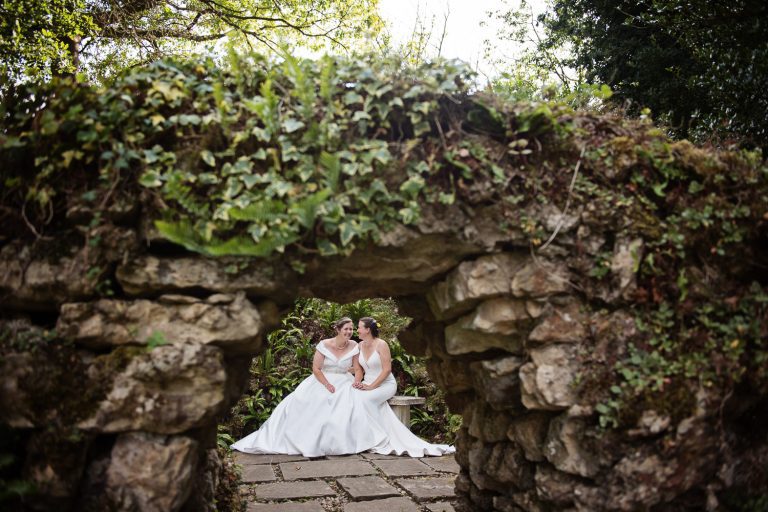 A secret garden at Cowley Manor. Looking through a gap in a wall you see the bride and bride having a giggle.