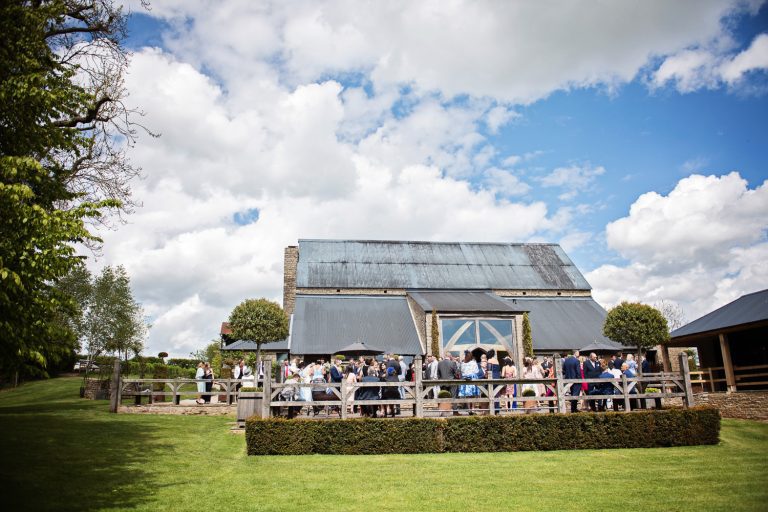 Exterior of Cripps Barn during a wedding reception. Wedding guests on the terraces chatting and mingling.