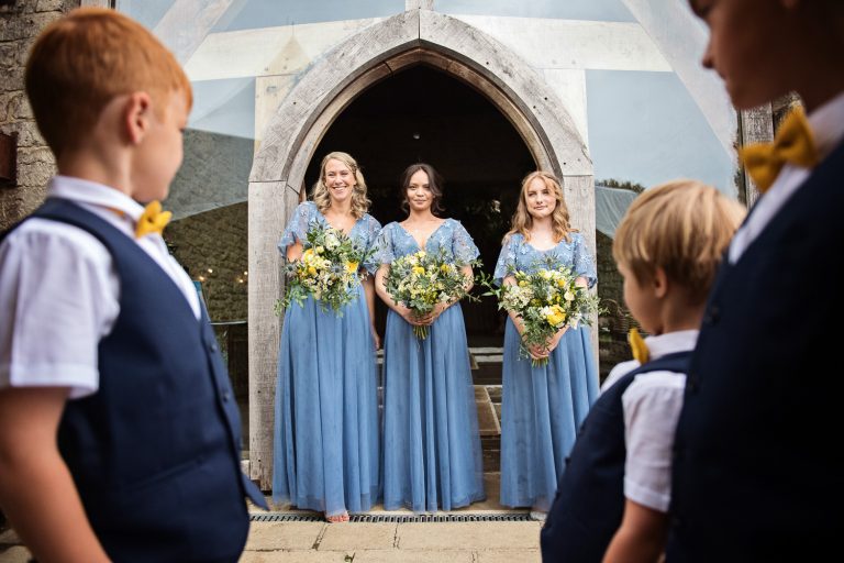 Bridesmaids line up outside the barn door, with the page boys watching them (and framing them!).