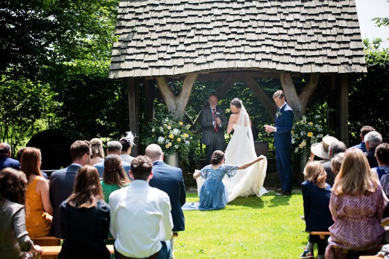 A bridesmaids pulls out and shapes the brides wedding dress during the outdoor ceremony at Cripps Barn.