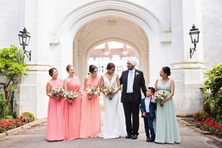 Bride and her bridal party stand together smiling in front of a large and impressive gated entrance.