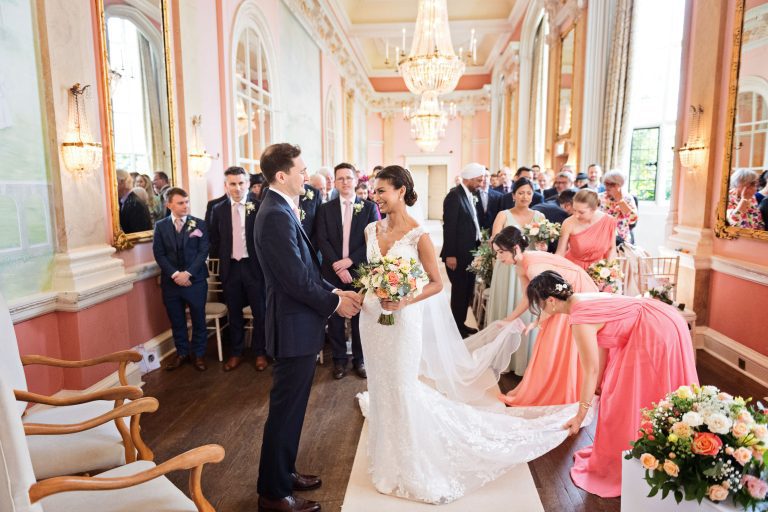 A bride greets her husband to be during their wedding ceremony at Danesfield House. Chandeliers and ornate fixings make this look luxurious