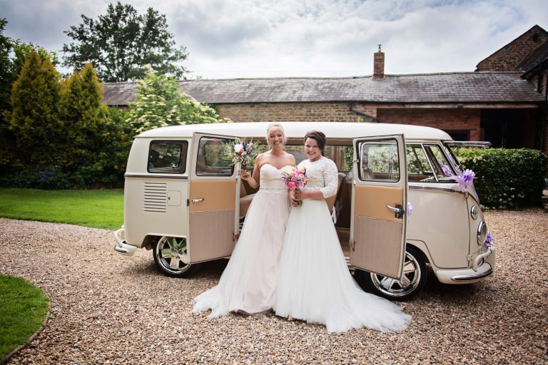 Bride and bride stand in front of a split screen VW in the grounds of Dodmoor House.