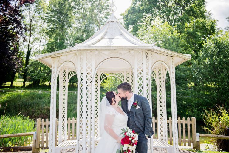 Bride and groom kiss in front of a pergola.