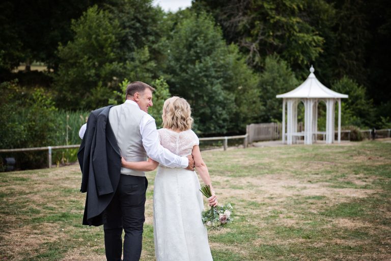 Bride and groom walking away, smiling at each other with a romantic hut in the foreground.