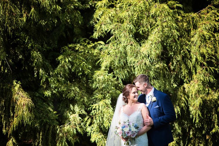 Bride and groom have a moment together in front of some conifers.
