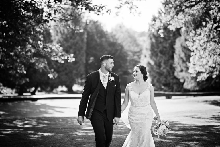 B&W image of a bride and groom holding hands as they walk in the grounds at Eastington Park