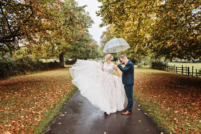 Autumnal image (lots of leaves on the floor), with a bride and groom (holding an umbrella)
