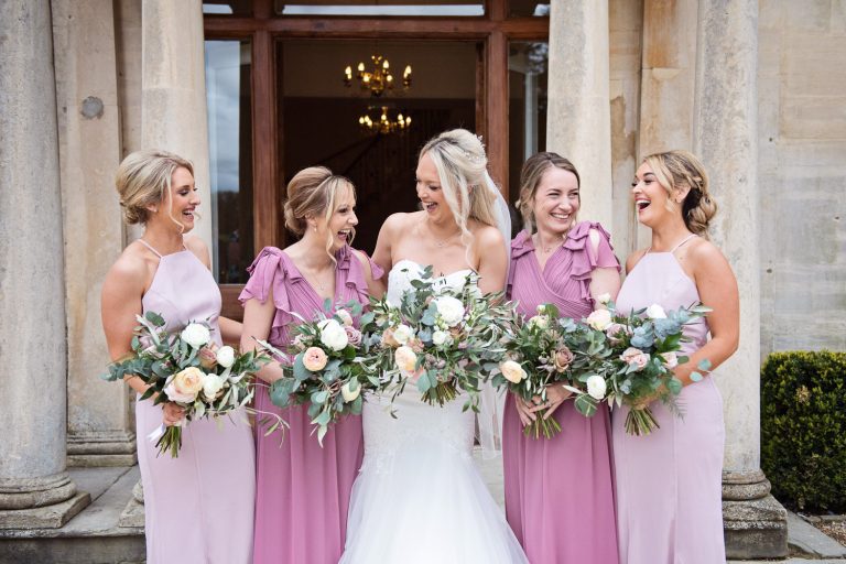 Bride and bridesmaids smiling and laughing outside the front of Eastington Park