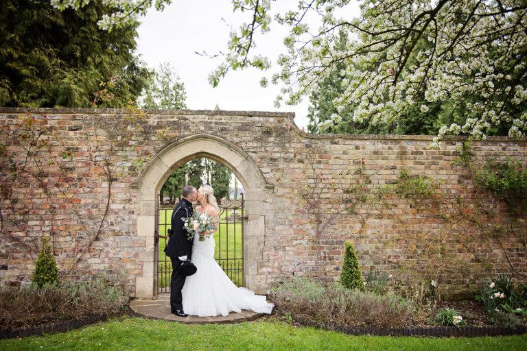 Bride and groom kiss underneath the gate in the walled garden at Eastington Park