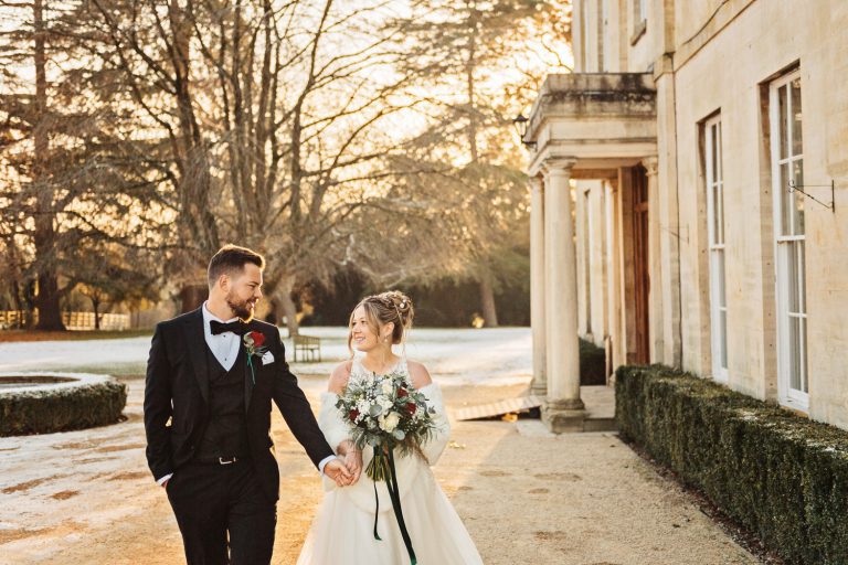 Gorgeous winter photo of bride and groom walking hand in hand during the golden hour at Eastington Park. Snowy backdrop.