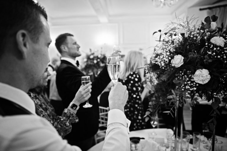 B&w photo of wedding guest raising their glass in celebration at the end of speeches at Eastington Park.