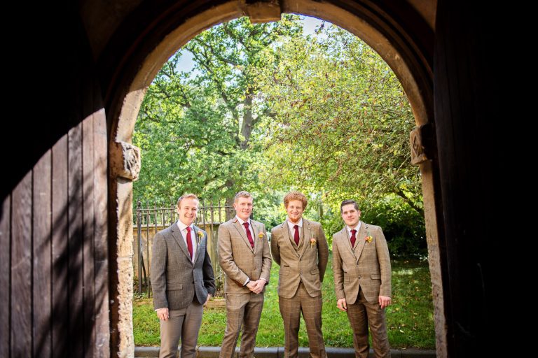 Groomsmen stand underneath arch. Look cool.