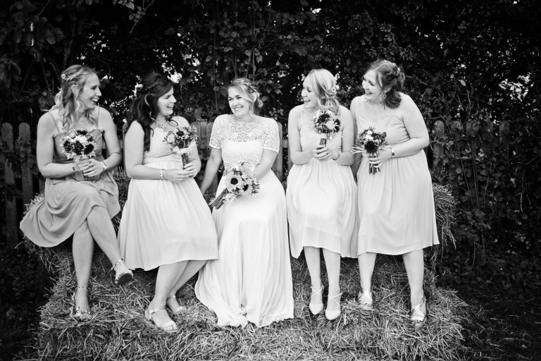 Relaxed, candid photo of bride and bridesmaids sitting on a bail of hay