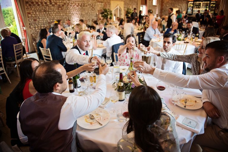 Wedding breakfast in full flow with wedding guests chatting and smiling and cheering each other as they do shots.