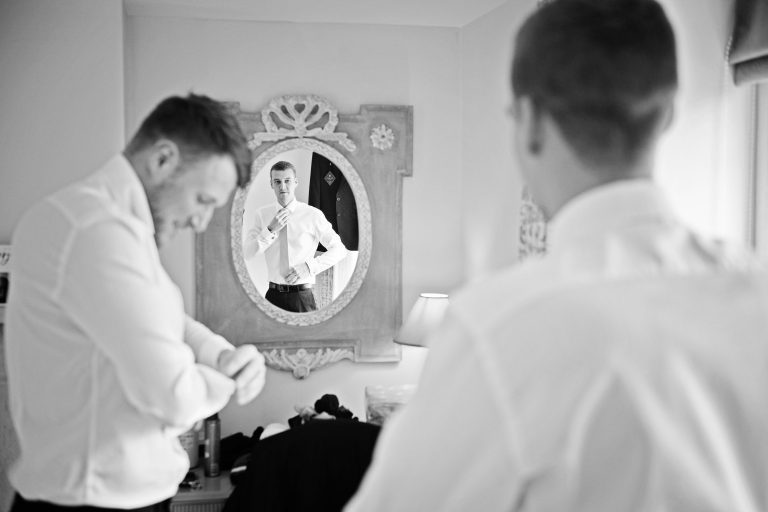 Candid photo of groom adjusting his tie in the mirror at Great Tythe Barn.