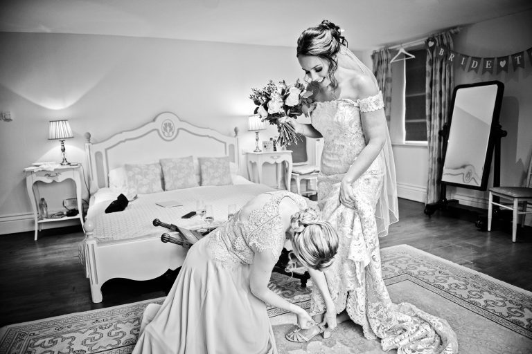 B&W photo of a bridesmaid doing the buckle up on the brides shoes.