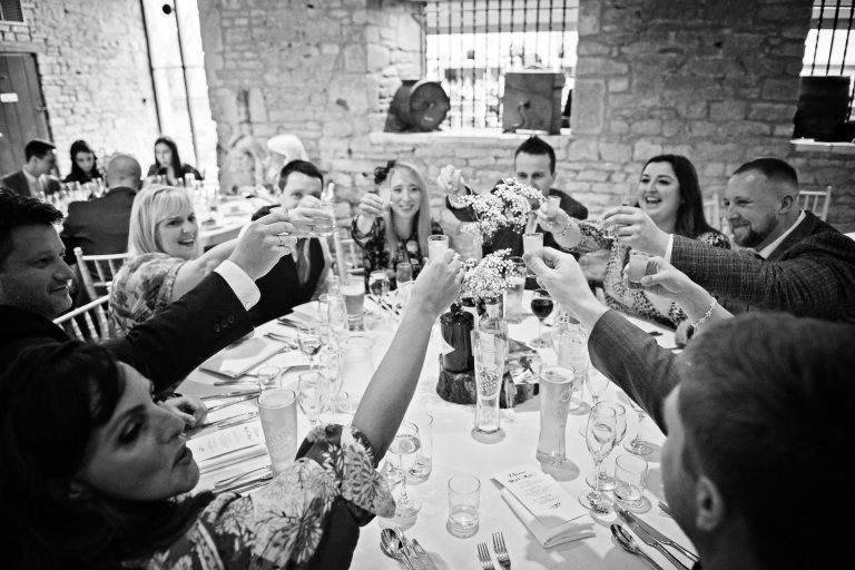 B&w image of wedding guests cheering each other at Great Tythe Barn, Tetbury.