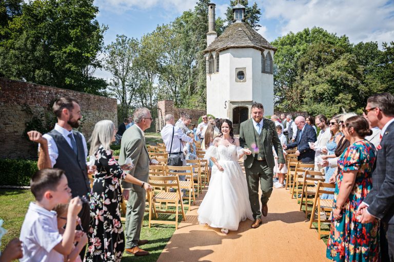 Bride and groom having confetti and bubbles being thrown/blown at them in the gardens of Homme House.