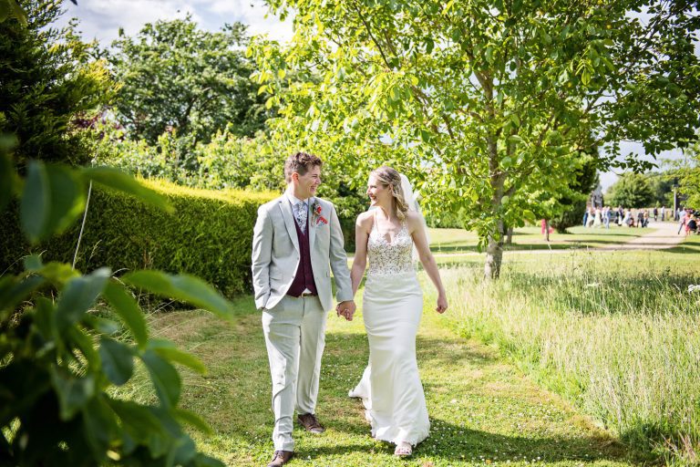 Bride and groom walk hand in hand in the gardens of Huntsmill Farm.