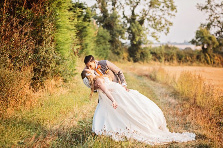 Bride and groom dipping and kissing in a field.
