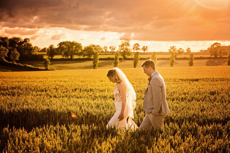 Bride and groom walk through a wheat field during golden hour.