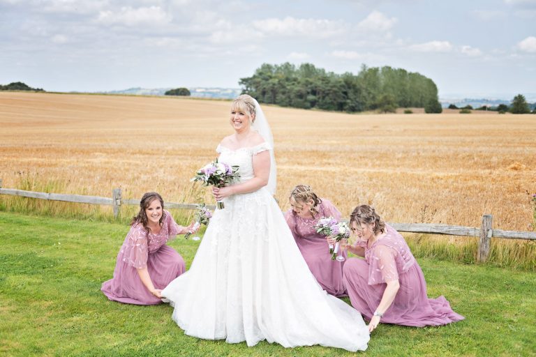 Bridesmaids pull out the brides dress with the rolling Cotswold countryside.
