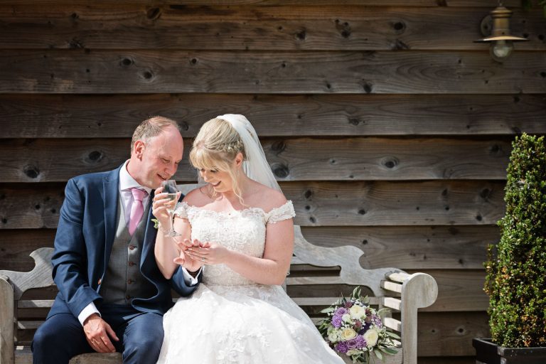 Newly married Bride and groom sit on a bench and admire each others wedding rings.