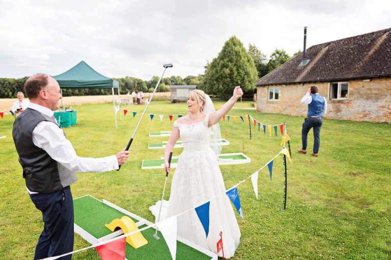 Fun photo of the bride and groom playing pitch and put golf. The bride has just won and is fist bumping the air.