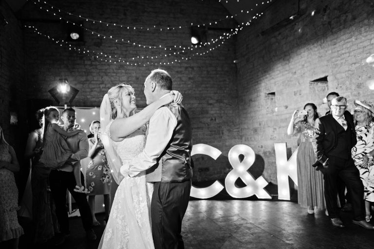 B&W image of Bride and groom doing their first dance with their friends and family watching.
