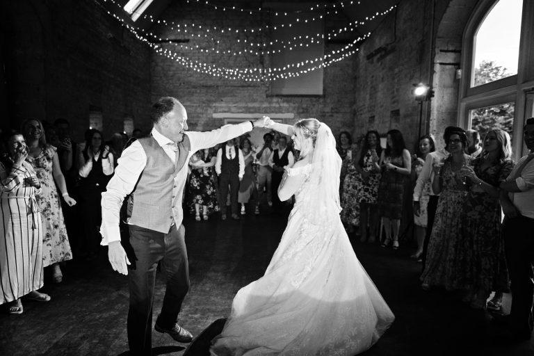 B&W image of Bride and groom doing their first dance with their friends and family watching.