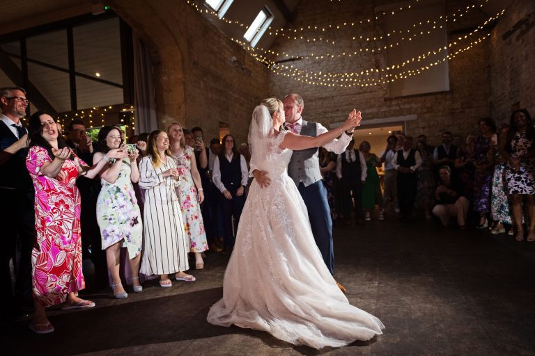 Bride and groom do their first dance with their friends and family watching.