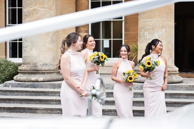 Photograph of bridesmaids shot through the ribbon of the wedding car.
