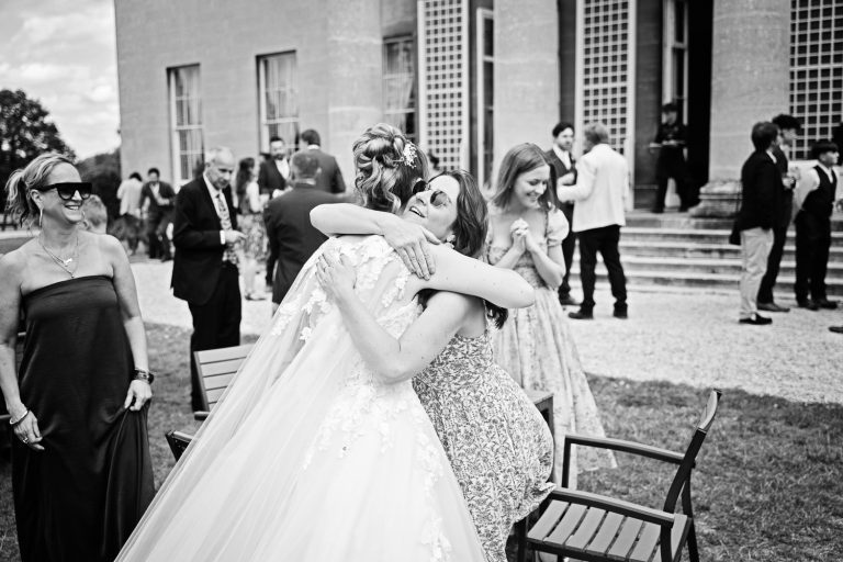 B&W documentary photo of bride hugging a wedding guest with friends dotted around them.