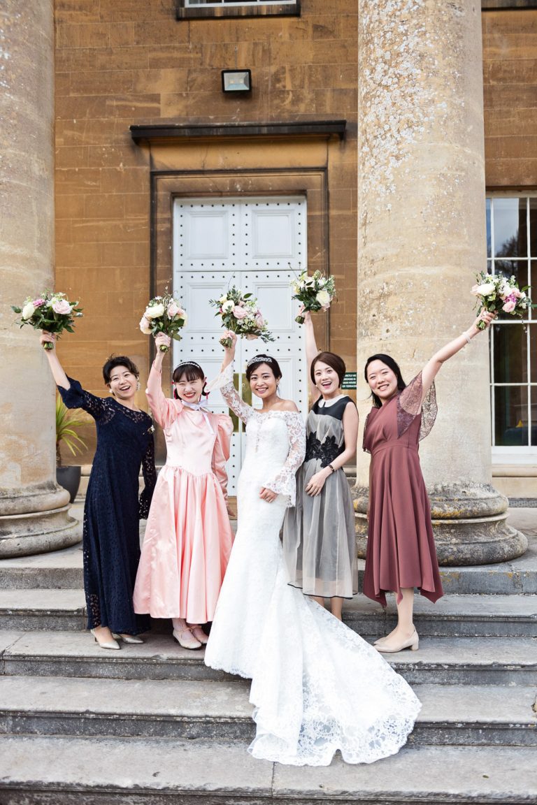 Fun portrait photo team bride on the steps holding their flowers up in the air.