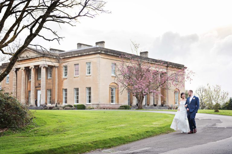 Bride and groom walk together down the drive with Leigh Court in the background.