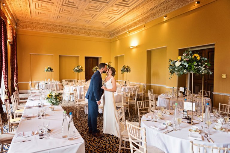 Bride and groom kiss in the middle of wedding breakfast room.