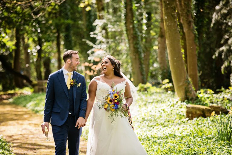 Bride and groom walk hand in hand relaxed through the stunning woodland at Spring time.