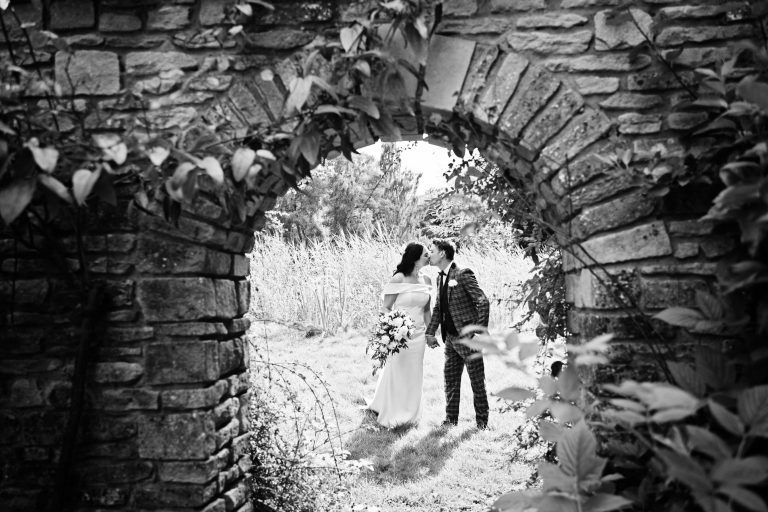 Bride and groom kiss. Photographed through a open (old) walled door entrance. B&W