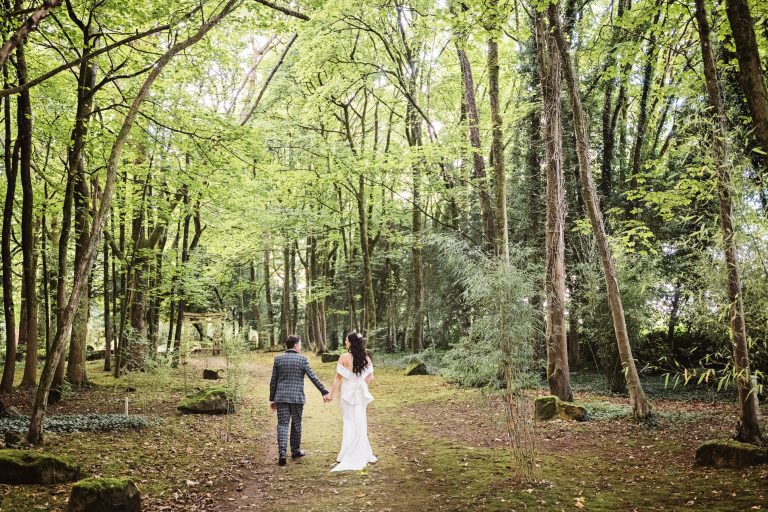 Bride and groom hold hands walking through the woodland at the Matara.