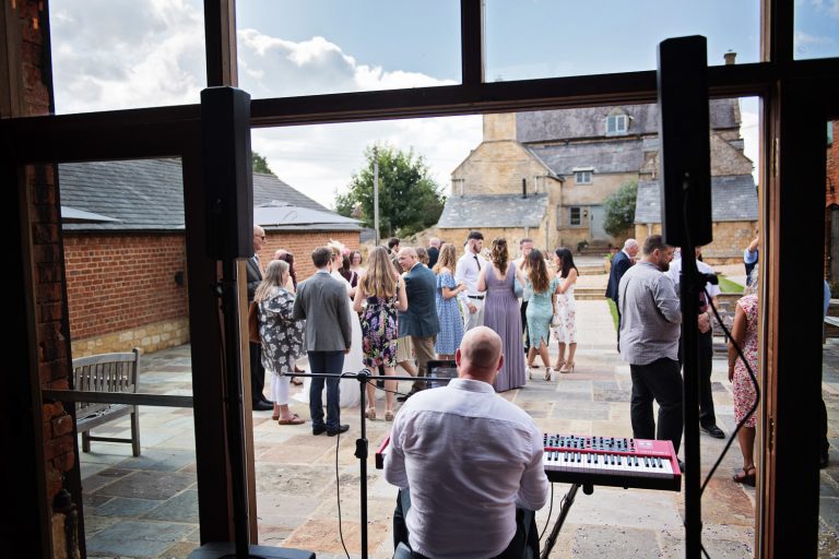A shot behind James Roscoe Pianist/Musician whilst he is doing his thing and entertaining wedding guests with his keyboard and singing in the doors of the barn at Mickleton Hills Farm.